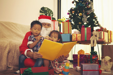 Obraz na płótnie Canvas Santa Claus is reading fairy tales to boy and girl.