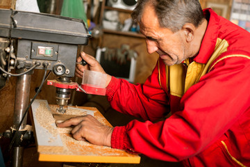 carpenter using drill press to mae hole in wooden plank