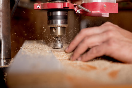 carpenter using drill press to mae hole in wooden plank