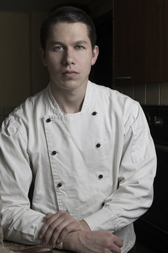 Portrait of nice and attractive man chef in uniform in his restaurant. Man chef standing in kitchen and posing to camera.