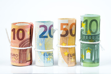 Several rolls of euro banknotes stacked by value from ten, twenty, fifty and one hundred euros isolated on white background.