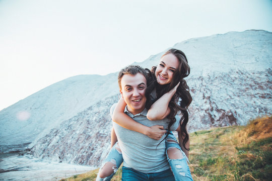 Young couple in love is resting together near the lake and mountains, beautiful caucasian woman and man fell in love, tenderness and hugs, straight couple against the beautiful background