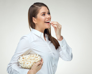 Woman wearing white shirt eating pop corn from glass bowl.