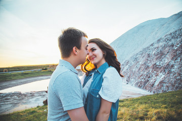 Young couple in love is resting together near the lake and mountains, beautiful caucasian woman and man fell in love, tenderness and hugs, straight couple against the beautiful background
