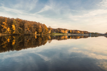 Fototapeta premium Beautiful lake and colorful forest in autumn evening light. Beautiful forest of colorful autumn trees reflecting in calm lake in Duchonka (Slovakia). Fall season. Scenic view of pond in autumn.