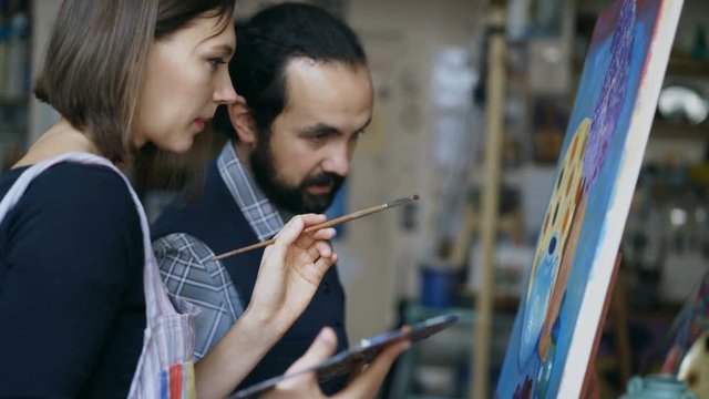Skilled artist teacher showing and discussing basics of painting to student at art-class