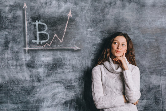 Girl watching the chart of bitcoin exchange rate drawn on black chalkboard with chalk