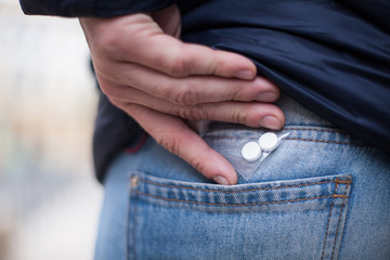 A man hides a dose of drugs in the back of his jeans pocket.