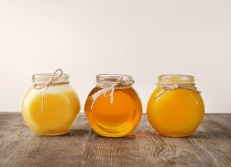 Aromatic honey in glass jars on table against light wall