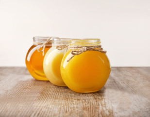 Aromatic honey in glass jars on table against light wall