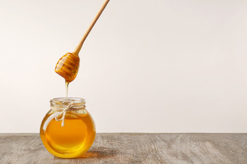 Pouring aromatic honey into jar on table against light wall