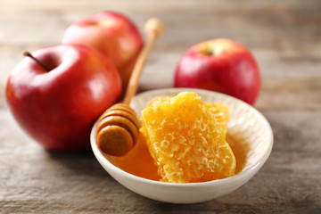 Honeycomb in bowl and apples on wooden table