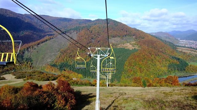 4K UHD footage of ski lift or elevator going down with empty seats over colorful autumn mountain landscape background