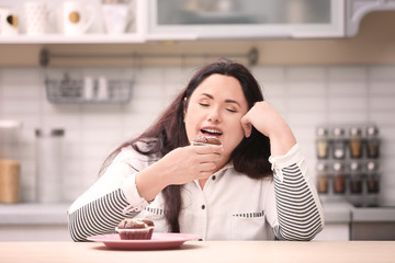 Overweight young woman with unhealthy food at table in kitchen
