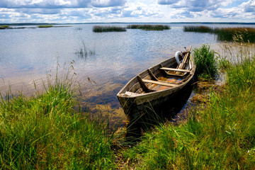 A boat near the shore. Blue sky, water, grass. The concept of fishing, recreation, travel.