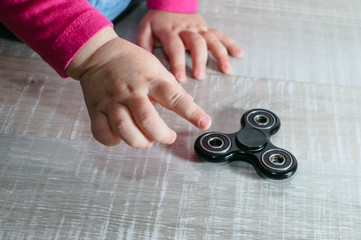 Child sitting on wooden playground and considering with fidget spinner gadget