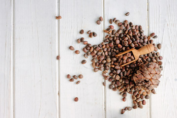 Top view of pine nuts in a wooden scoop over a white wooden background.