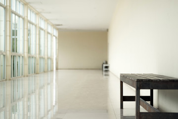 Empty walkway in building hall perspective with long white wall on right side and long windows with light on left and granito tiles floor in minimalist.