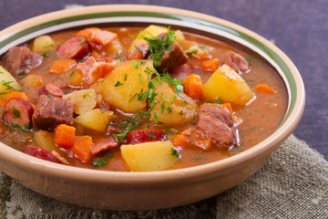 Stew, made with beef, bacon, sausages potatoes, carrots and herbs. Goulash soup bograch in a bowl. Hungarian dish