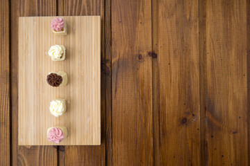 Small multicolored sweet cakes with cream on a wooden background.