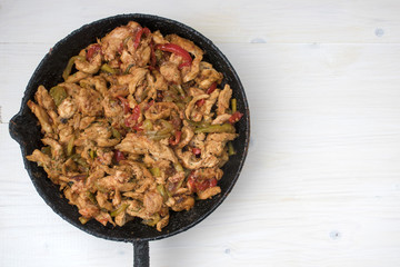 Chicken stew with red and green pepper, with red onion, pickled cucumber and spices in a frying pan.
