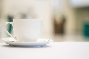 White cup of coffee placed on white table with blurred people have seminar in meeting room background.