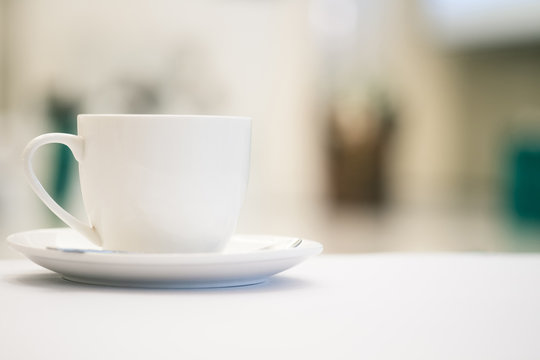 White Cup Of Coffee Placed On White Table With Blurred People Have Seminar In Meeting Room Background.