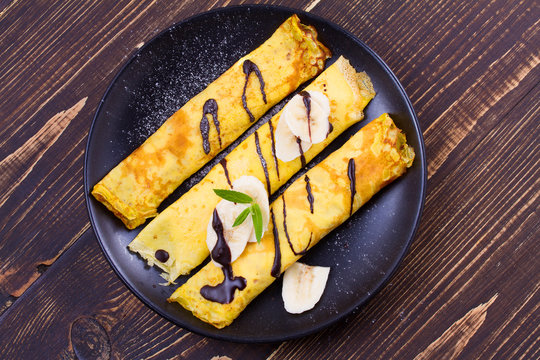 Wrapped thin pancakes  with filling, served with bananas, chocolate and mint