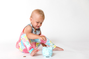 Smiling toddler girl is giving one of the coins to the saving piggy bank