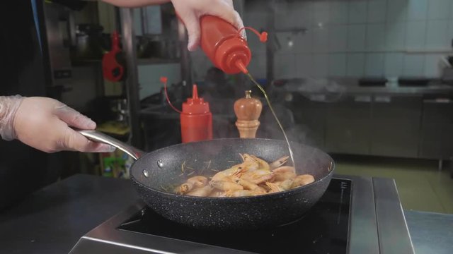 Chef frying shrimps on a pan, pouring sause and tossing it at commercial restaurant kitchen, close-up slow motion.