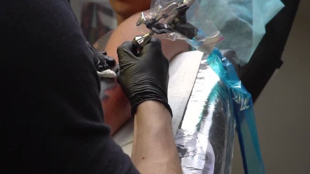 Tattoo parlor guy with Bluetooth headset makes a tattoo to another guy