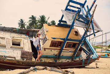 young female poses at old fishing wreck ship on ocean beach sri lanka