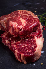 Two Raw beef steaks with spices on dark stone background close up