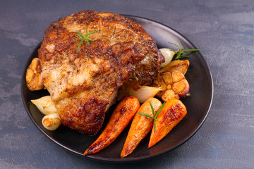Roasted ham with rosemary, carrots and garlic on black plate