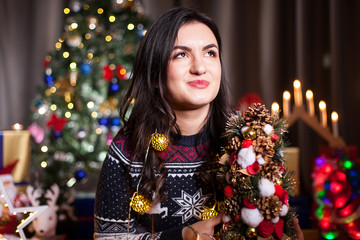 Happy young woman holding a mini Christmas tree in hands in Christmas decorated interior