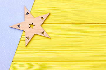 Fototapeta na wymiar Wooden Christmas star and copy space. Carved wooden Christmas ornament with craft paper on yellow wooden background, space for text.