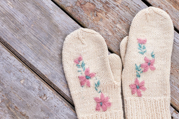 Pair of beautiful female mittens. Women knitted white gloves with a flowers embroidery on old wooden background. Cute present for New Year.