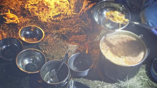 A young person prepares a hot meal in a cauldron on a fire outdoors