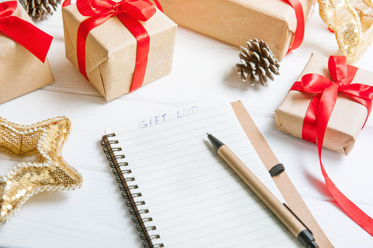 Close up List of gifts for Christmas. Drawing up a list of gifts. presents in kraft paper vintage white wooden background. pencil, notebook. Selective focus