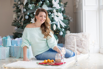 Young woman sitting in a room with a Christmas tree and gift boxes in the background. Blonde women smiling and having breakfast