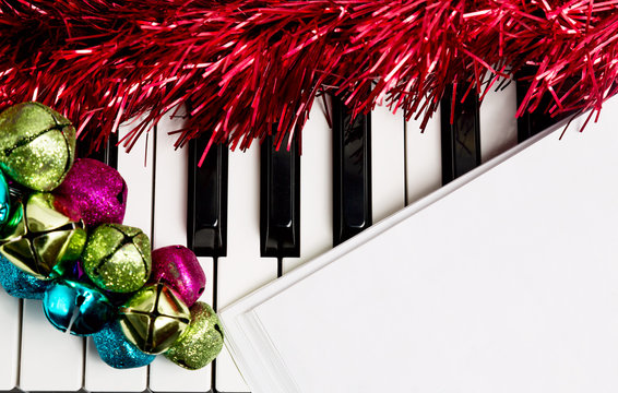 Christmas music concept. Blank paper on the piano with jingle bells and red tinsel