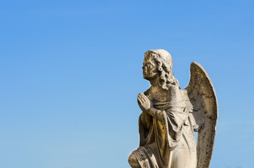 Fototapeta na wymiar Praying angel pray to God public sculpture on the cemetery with blue sky background