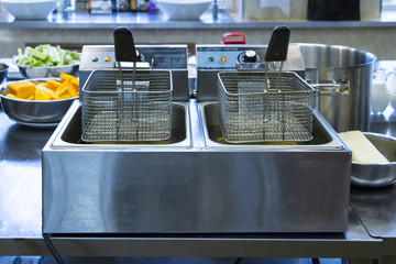 Professional fryer - machine for deep cooking in fat - in kitchen interior on metal table. Selective focus.