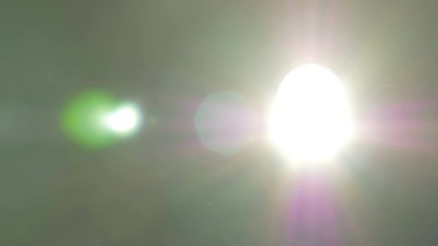 The glare of stage lights is filmed as they emmit their lights directly into the camera. Pan right. Close up.