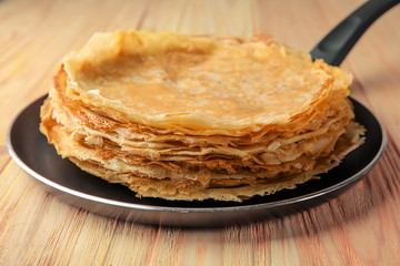 Pan with delicious thin pancakes on wooden table