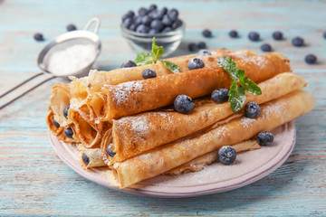 Plate with delicious rolled pancakes and berries on wooden table
