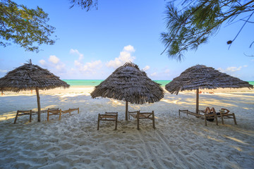 Wooden deck chairs and umbrella on stunning tropical beach. Turquoise blue lagoon of Paje beach, Zanzibar, Tanzania.