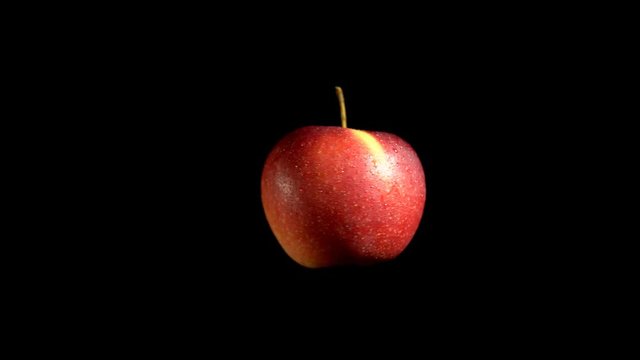 Close-up rotation red apple covered by drops of water. Fresh juicy fruit isolated on black background.