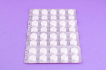 Packs of white pills packed in blisters with copy space on purple background. Focus on foreground, soft bokeh