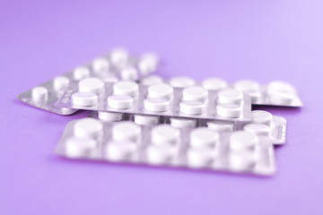Packs of white pills packed in blisters with copy space on purple background. Focus on foreground, soft bokeh